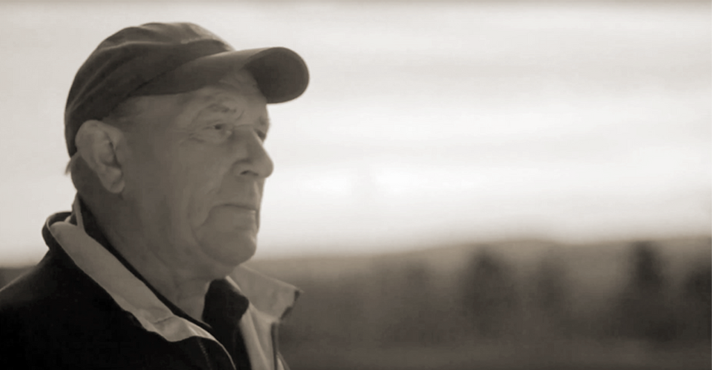 An older man wearing a baseball cap and looking off into the distance.